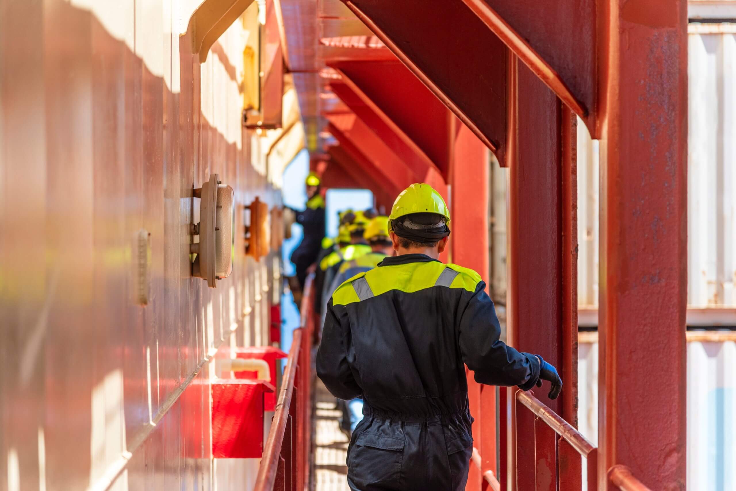 Deck,Officer,Seen,From,Behind,Walking,Between,Containers,And,Superstructure