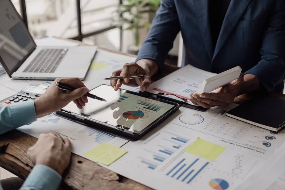 Documents, graphs and financial or marketing charts and there is a laptop and digital tablet on the table