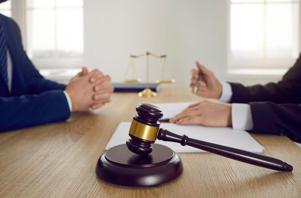 Judge's gavel against background of judge and lawyer who are discussing legal case with documentary contract